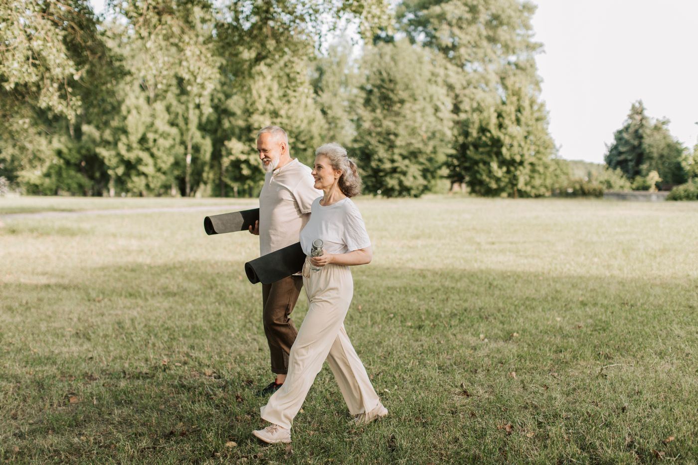 Senior couple walking across a park carrying yoga mats